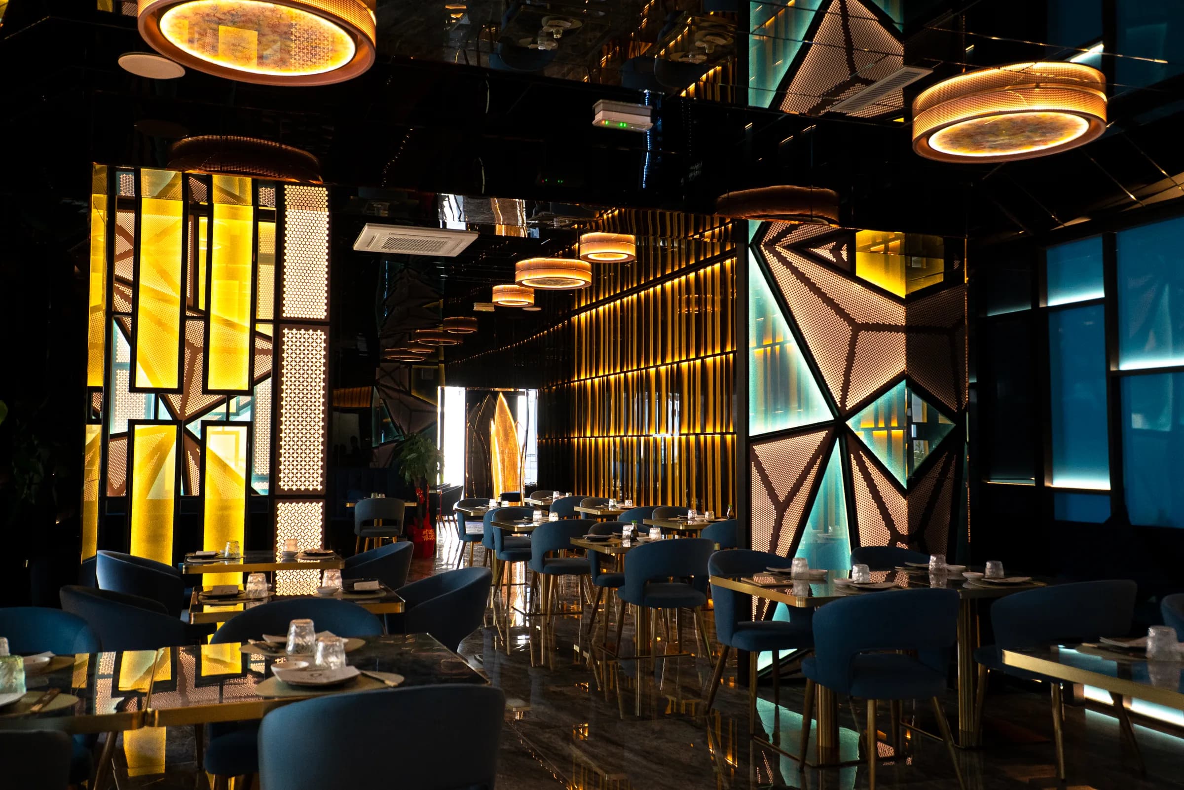 La sala di SushiSound: tavoli blu, pareti di luce gialla e pannelli geometrici illuminati