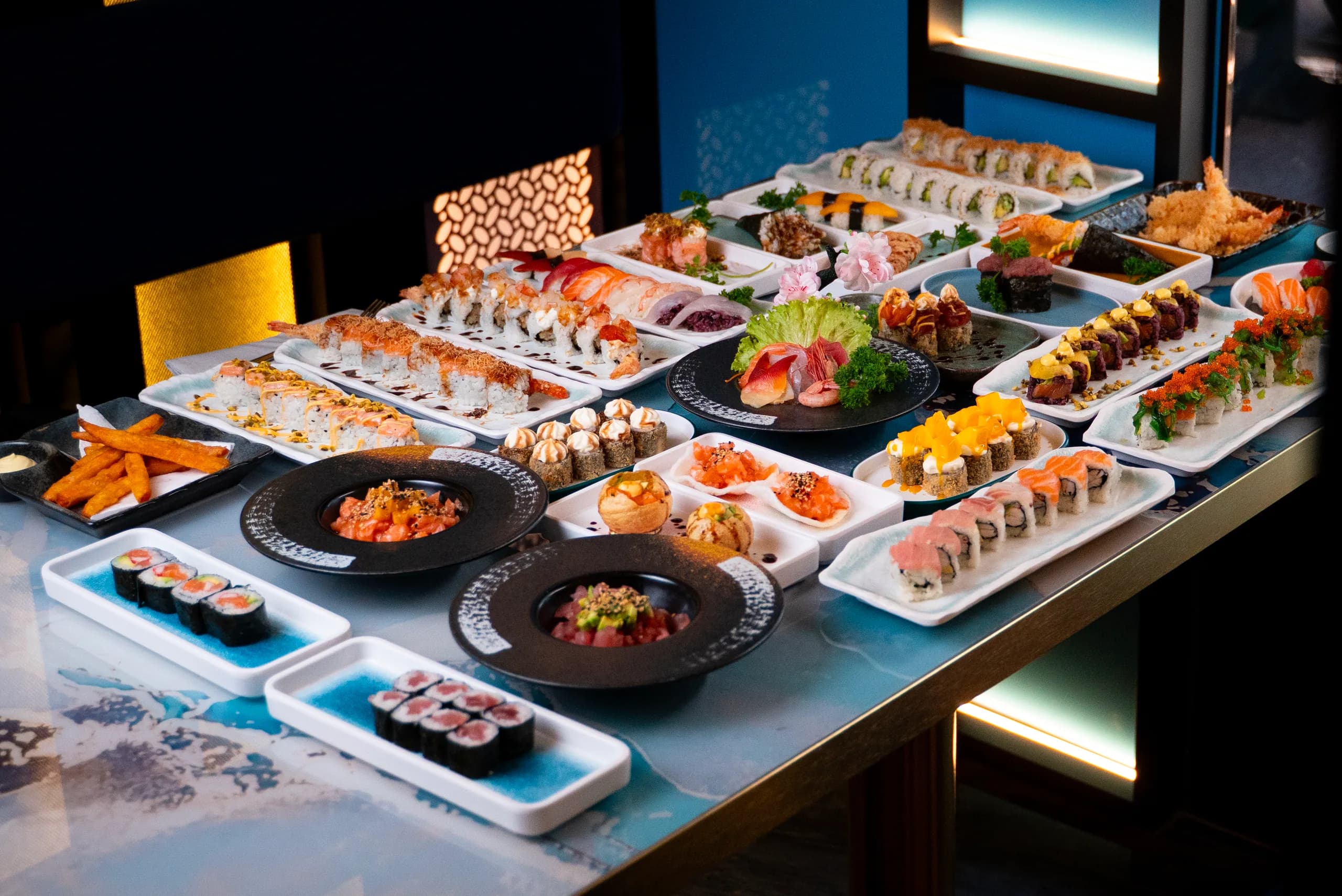 Un tavolo apparecchiato con decine di piatti di sushi, roll, tartare e tempura